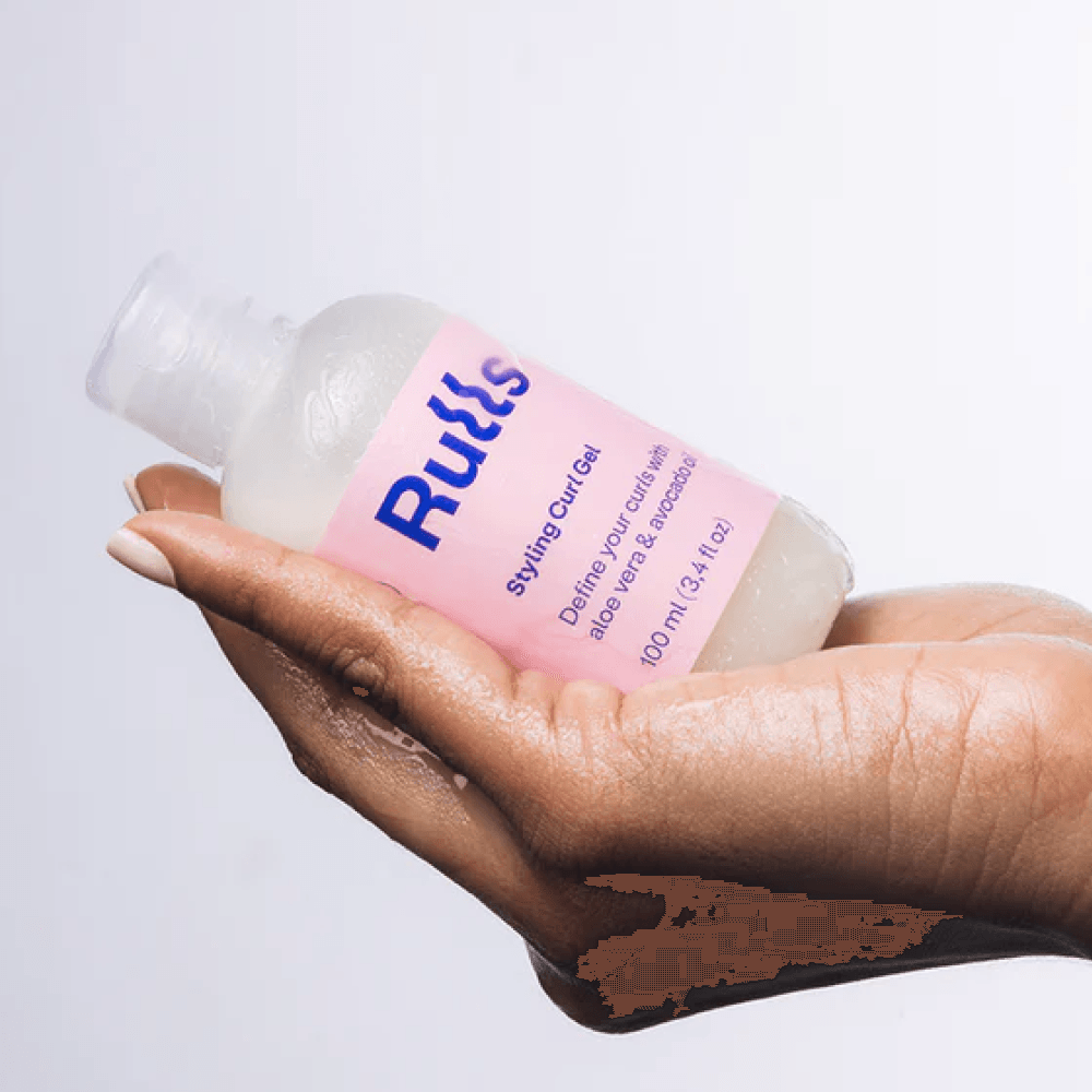 Hand holding a clear Rulls Styling Curl Gel bottle with a pink label.